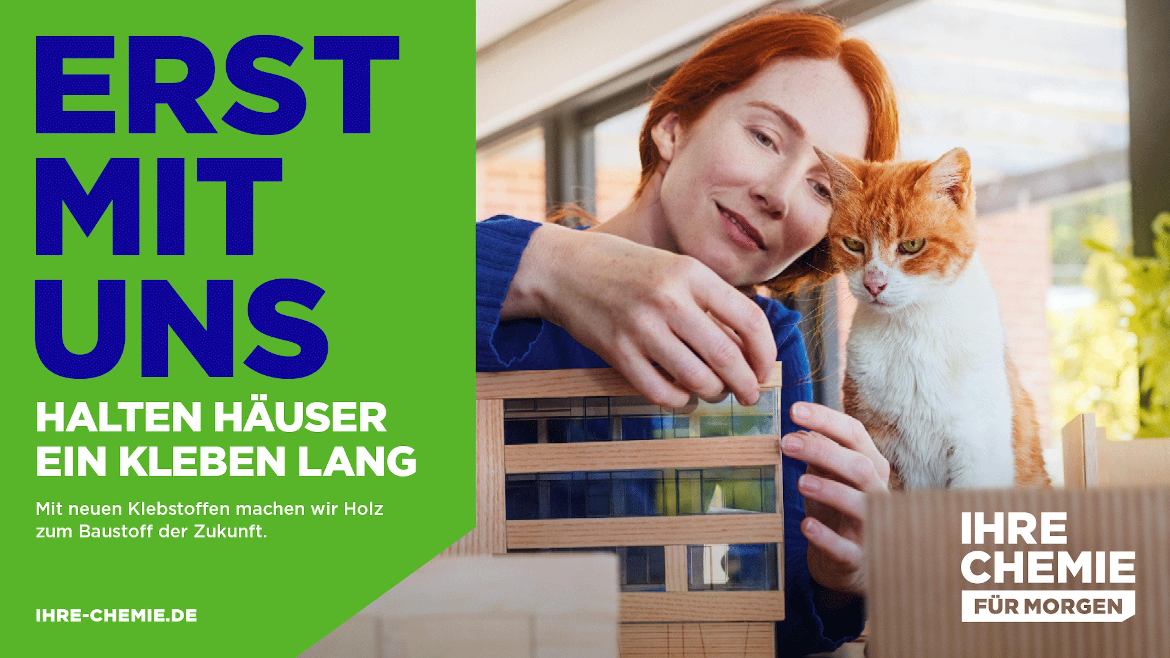 Kampagnenmotiv "Erst mit uns halten Häuser ein Kleben lang" mit einer Frau und Katze beim Holzmodellbau.
