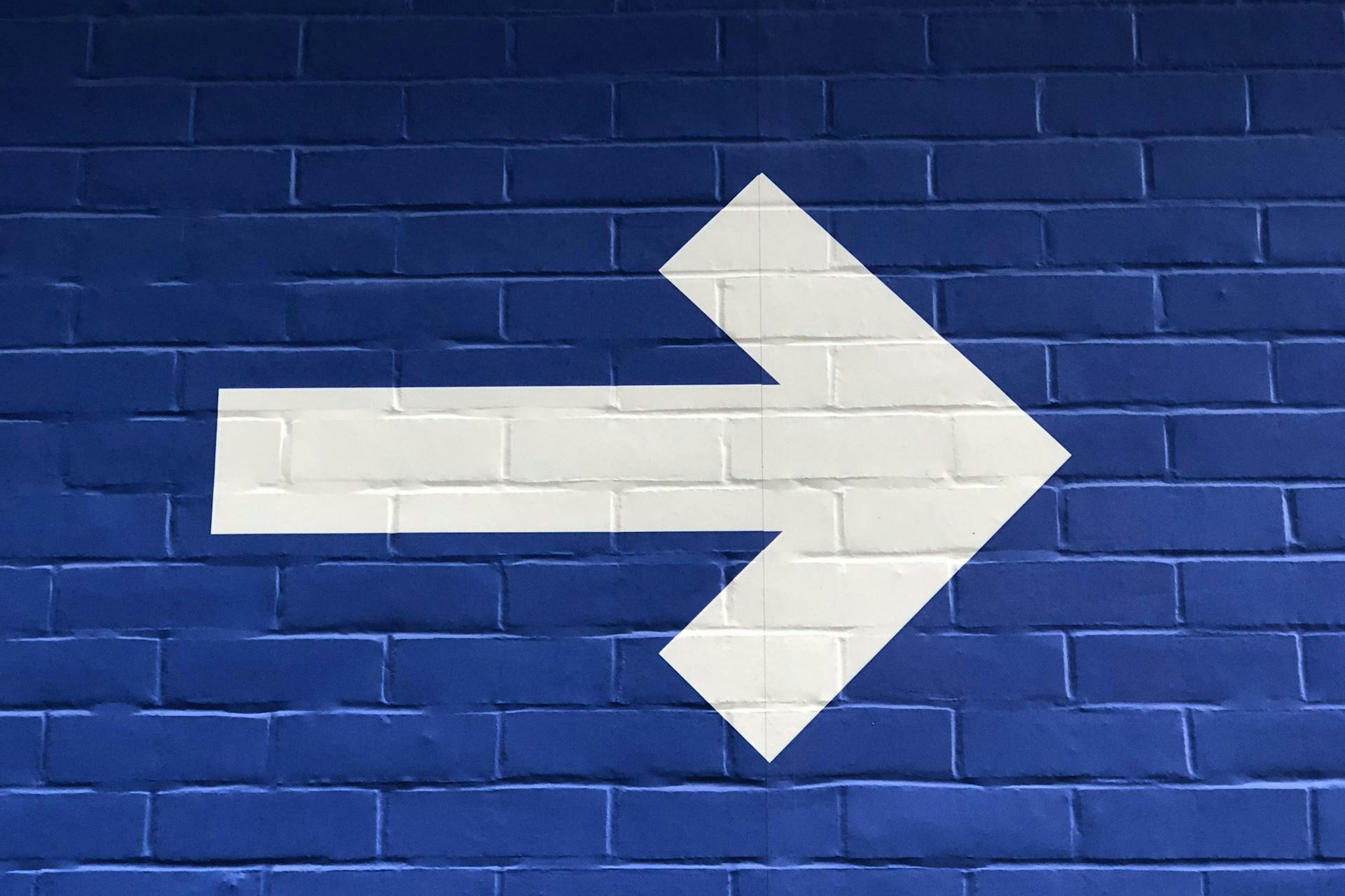 White arrow on a blue brick wall. Photo by Nick Fewings.