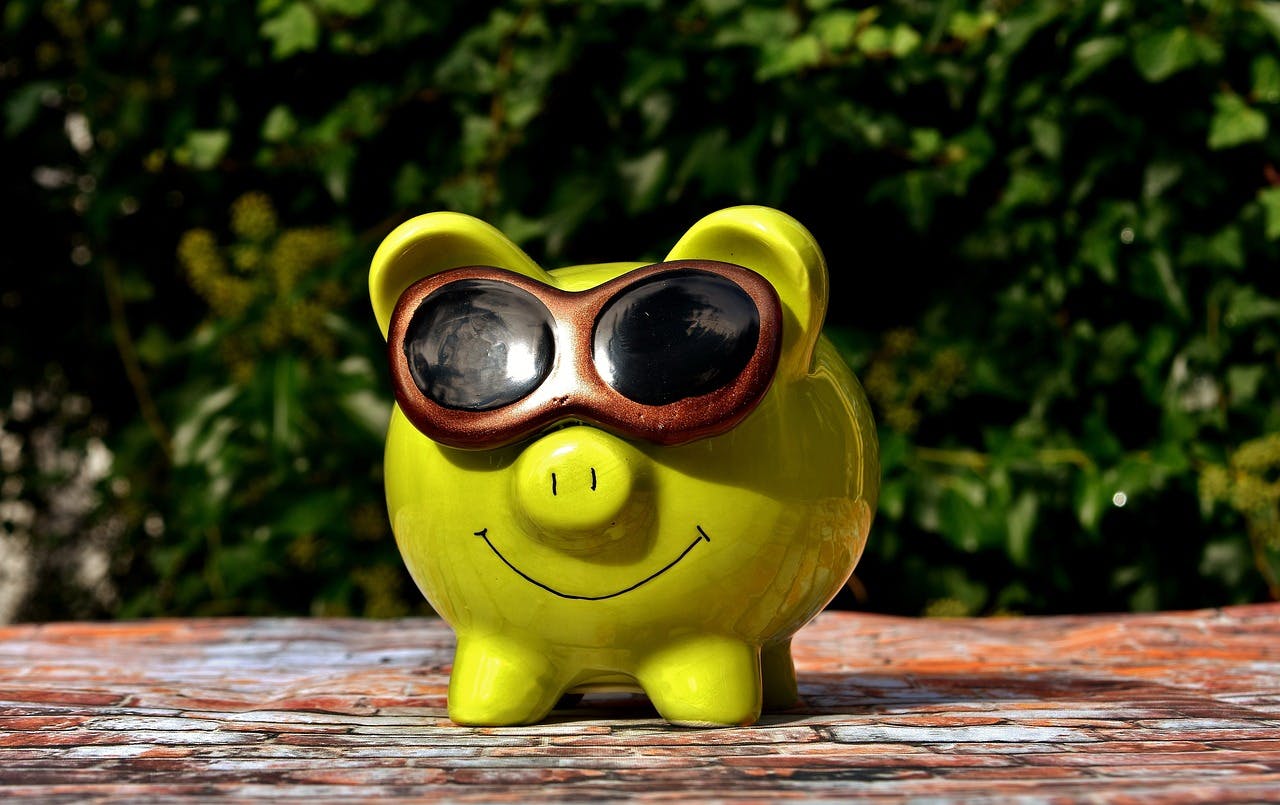 A green smiling piggy bank wears a pair of sunglasses.