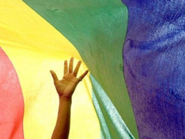 A hand stretches in front of a rainbow flag