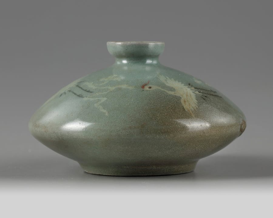 A Korean slip-inlaid celadon-glazed ‘cranes’ oil bottle. The compressed jarlet is inlaid with white, red, and black clays with cranes with open wings in flight amongst clouds. Photo © Oriental Art Auctions