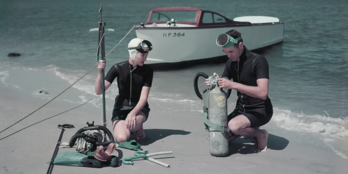 Man and woman adjusting scuba gear on the beach. Photo by Harold M. Lambert via Getty Images (detail)