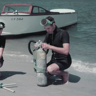 Man and woman adjusting scuba gear on the beach. Photo by Harold M. Lambert via Getty Images (detail)