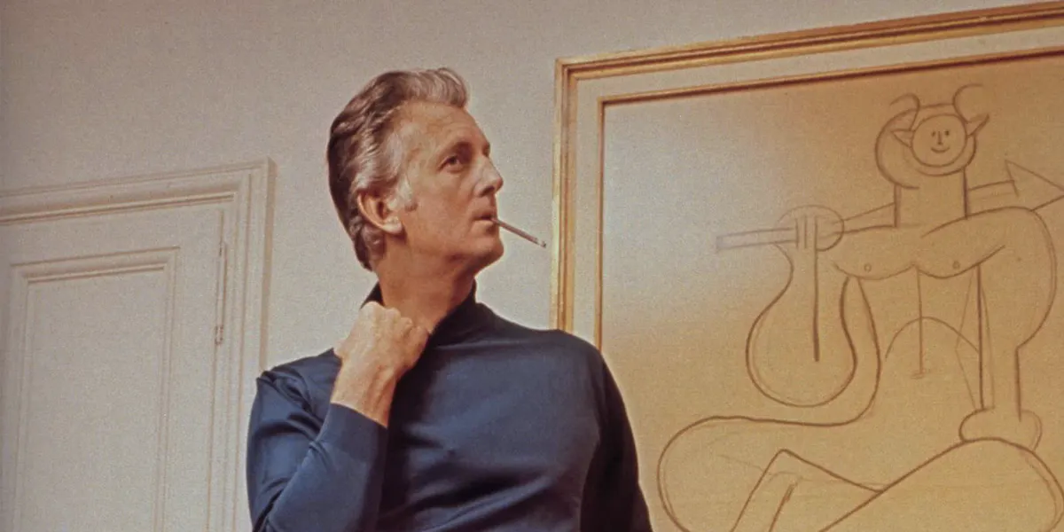 In the Paris salon, in front of a Picasso drawing, designer Hubert de Givenchy stands wearing evening trousers in a nubby silver brocade with a navy turtleneck, all by Givenchy [detail]. Photo by John Cowan/Conde Nast via Getty Images