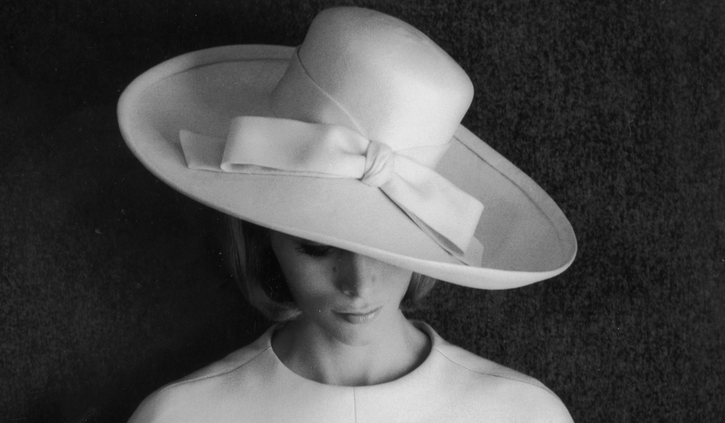 Un due pezzi in lino bianco disegnato da Yves Saint Laurent. Giacca con maniche lunghe fino al polso, senza colletto, tasche applicate. L'outfit è indossato con un cappello a tesa larga ed è parte della "Collezione Boutique". Foto di Barry Lategan / Getty Images