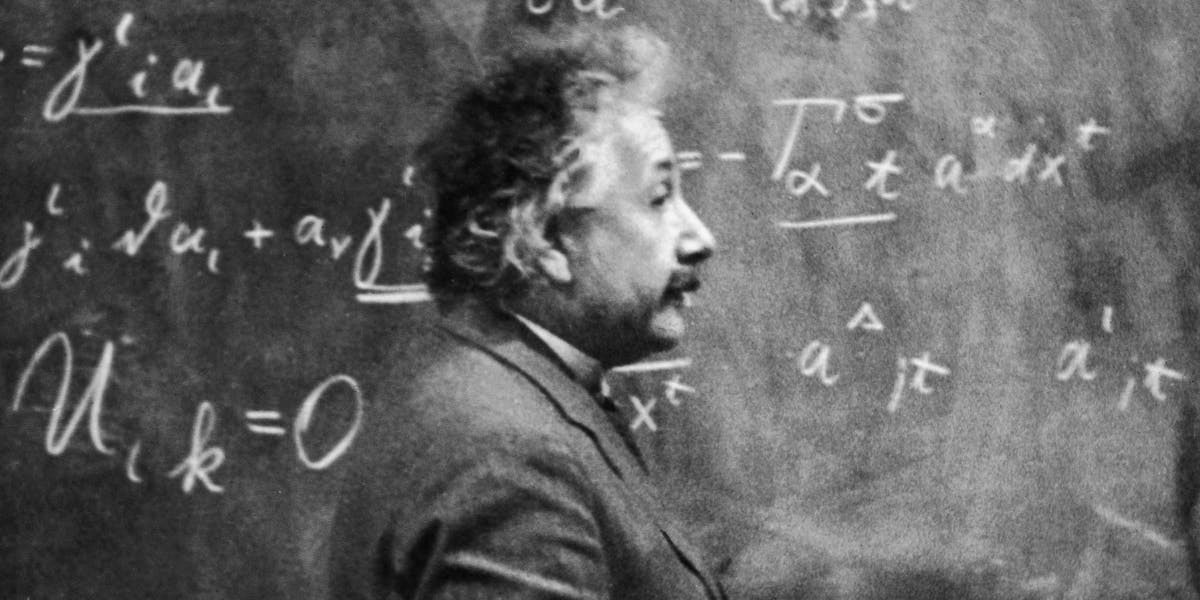 Albert Einstein standing beside a blackboard with chalk-marked mathematical calculations written across it. Photo © Hulton Archive/Getty Images (detail)