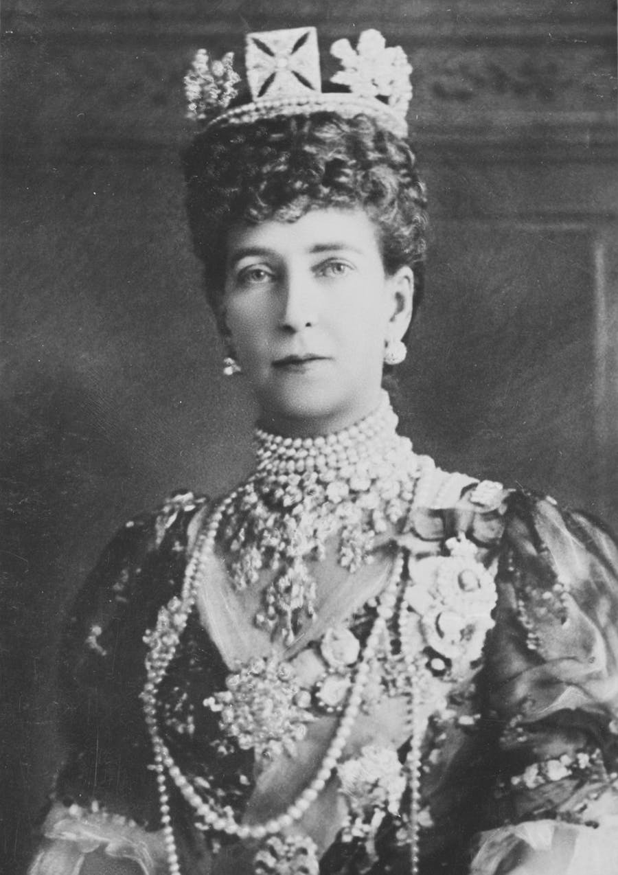 Bust-length formal portrait photograph of Queen Alexandra wearing King George IV's Diamond Circlet, Royal Family Orders, crown and other pieces of jewelry. Public domain image