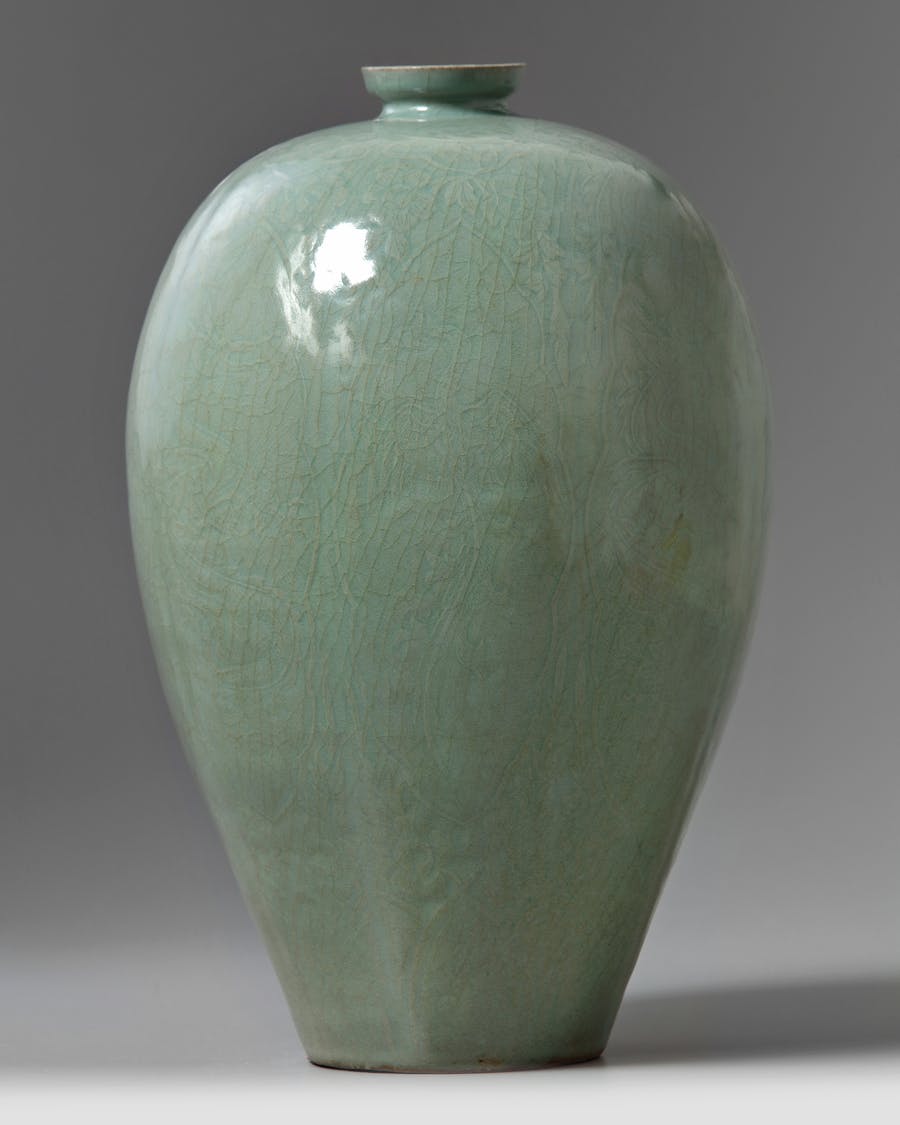 A large Korean celadon-glazed ‘dragon and phoenix’ maebyeong. The vase is lightly lobed and finely decorated with carved design of foliate petals enclosing alternating dragons and phoenixes, surrounded by flower scrolls, all below a ruyi-head to the rim and lappets to the foot. The vase is covered in a translucent bluish-celadon glaze with some fine glaze crackles. Photo © Oriental Art Auctions