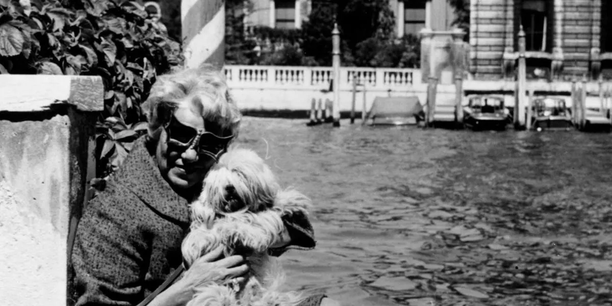 1964: Die amerikanische Kunstsammlerin und Millionärin Peggy Guggenheim (1898-1979) mit ihren Hunden vor ihrem venezianischen Palast aus dem 18. Jahrhundert am Canal Grande. Foto von Keystone / Getty Images (Detail)