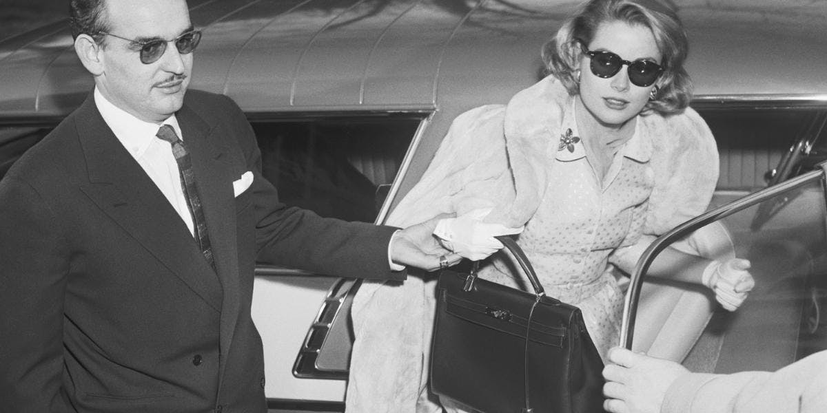 Prince Rainier III of Monaco helping his fiancée Grace Kelly out of a car. Kelly holds the style of Hermès handbag that was named after her (detail). Image Bettmann/ Contributor via Getty Images