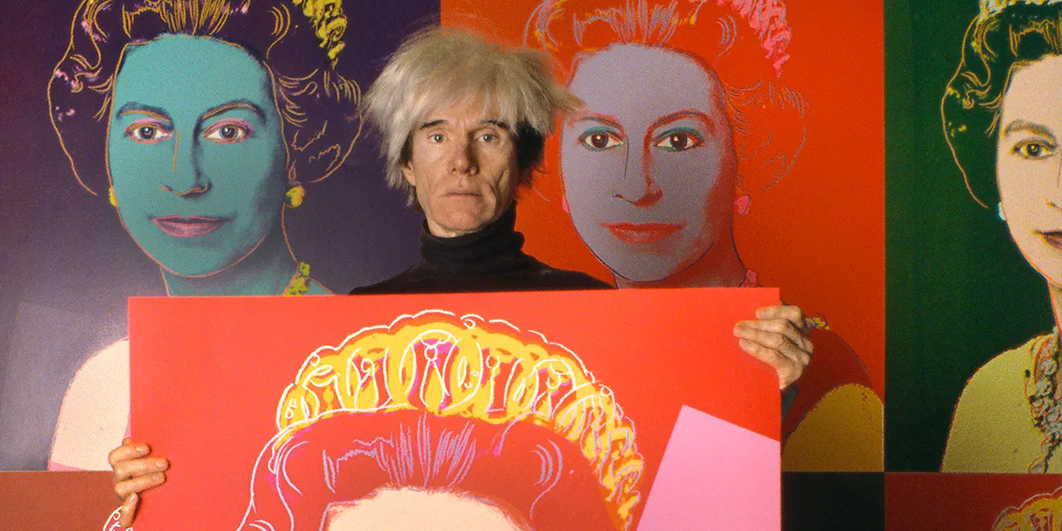 Ritratto dell'artista pop americano Andy Warhol (1928 - 1987) con in mano una serigrafia della monarca britannica Regina Elisabetta II nel suo studio, la Factory, New York, New York, 1985. L'immagine fa parte della sua serie Reigning Queens, altre delle quali sono appese alla parete dietro di lui. (Foto di Derek Hudson/Getty Images)(dettaglio)