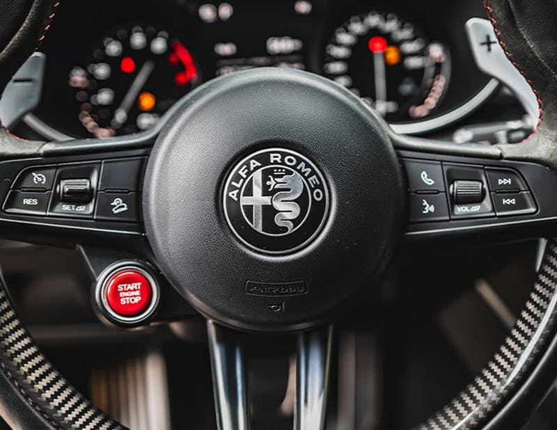 Detail of the steering wheel of an Alfa Romeo, with the logo featuring its characteristic snake. Photo by Łukasz Nieścioruk via Unsplash