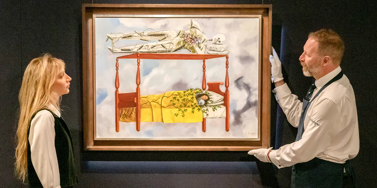 Due dipendenti di Sotheby's con l'autoritratto di Frida Kahlo "El sueño (La cama)" del 1940. Foto © Sotheby's (dettaglio)