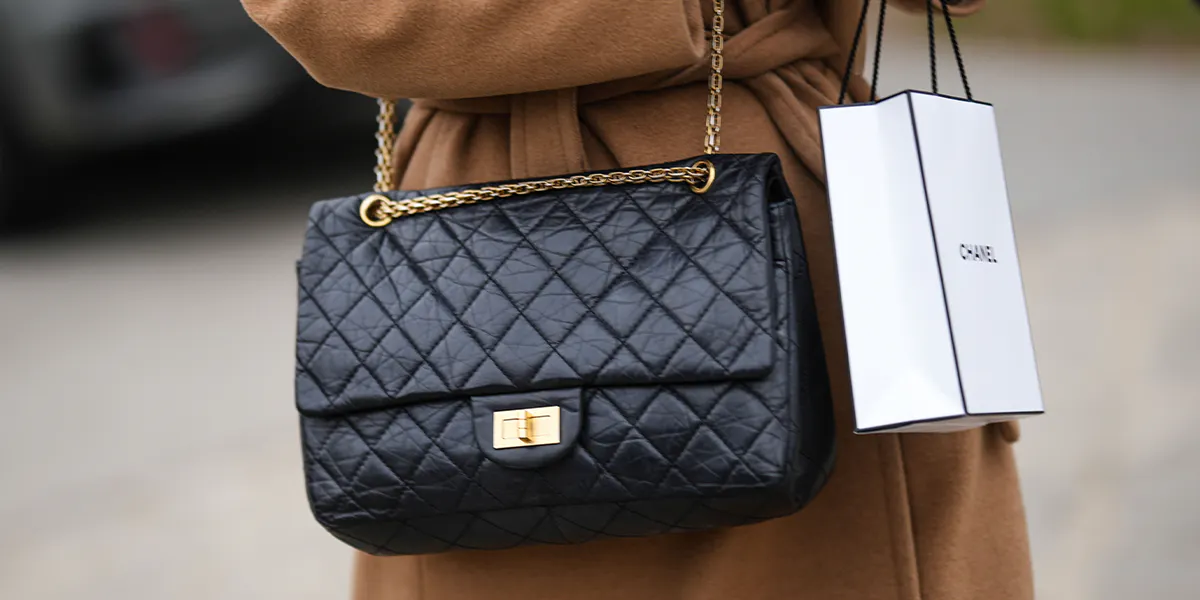 PARIS, FRANCE - JANUARY 24: A visitor outside Chanel wears a long, brown wool trench coat with a belt, a large, glossy black Chanel 2.55 shoulder bag, and a white Chanel tote bag during Paris Fashion Week - Haute Couture Spring/Summer, on January 24, 2023, in Paris, France. (Photo: Edward Berthelot/Getty Images) (Detail)