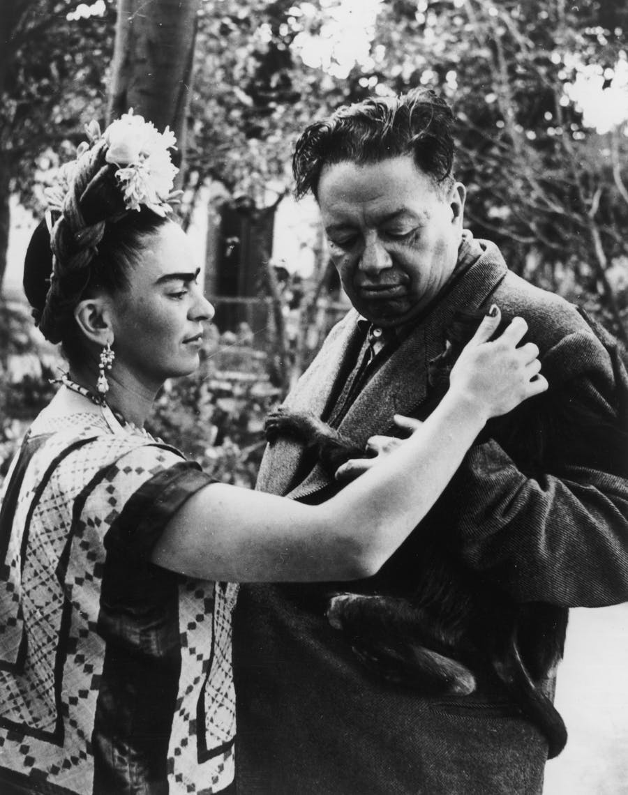 Circa 1945: Mexican artist Frida Kahlo (1907-1954) strokes a monkey, possibly Fulang-Chang, clinging to her husband's jacket, Mexican artist Diego Rivera (1886-1957). Photo by Wallace Marly / Hulton Archive / Getty Images