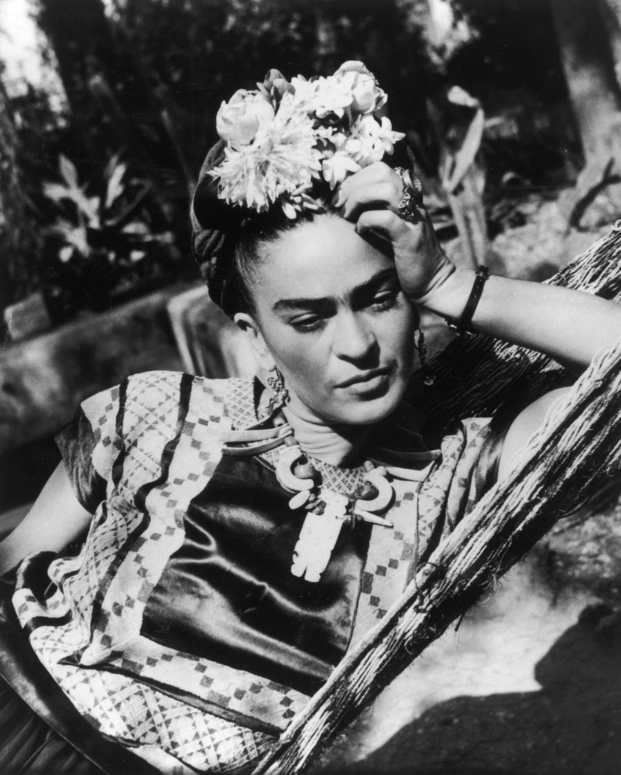 Frida Kahlo, in a traditional dress and topped with flowers, in a hammock. Image © Hulton Archive / Getty Images