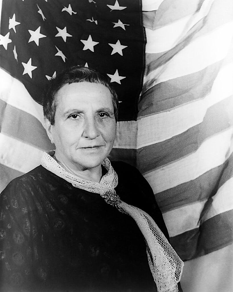 Portrait de Gertrude Stein, avec le drapeau américain en toile de fond, Carl Van Vechten, 4 Janvier 1935. Image du domaine public.
