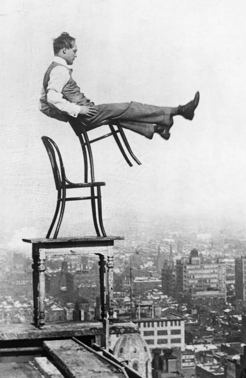 A man balancing on Thonet chairs, probably in the Czech Republic. Photo public domain
