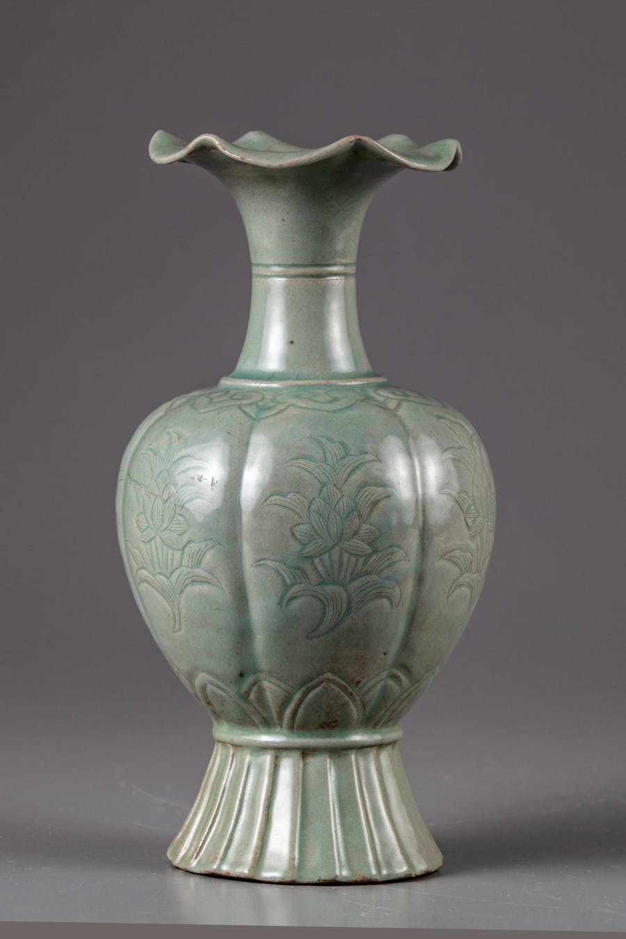A Korean celadon glazed vase, melon-shaped,  featuring the eight-petal flower mouth and incised parallel lines on the neck. The lobed sides are decorated with flower sprays, below a band of ruyi heads and plantain leaves to the base. All covered with a grey-green glaze. Photo © Oriental Art Auctions