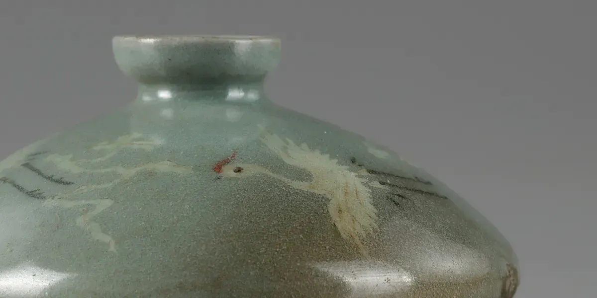 Koreanische Ölflasche mit Kranichmotiv, Schlicker-Intarsien und Seladonglasur. Das kleine Gefäß ist mit weißem, rotem und schwarzem Ton eingelegt und zeigt Kraniche mit gespreizten Flügeln, die zwischen Wolken fliegen. Foto © Oriental Art Auctions (Detail)