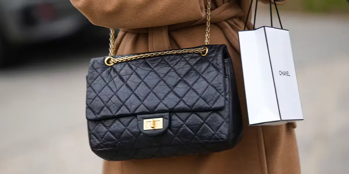 PARIS, FRANCE - 24 JANVIER : Une femme porte, devant la boutique Chanel, un long trench-coat en laine marron ceinturé, un grand sac à bandoulière 2.55 noir brillant de Chanel et un sac de courses blanc de Chanel, lors de la Fashion Week de Paris - Haute Couture printemps/été, le 24 janvier 2023 à Paris, en France. (Photo : Edward Berthelot/Getty Images) (Détail)