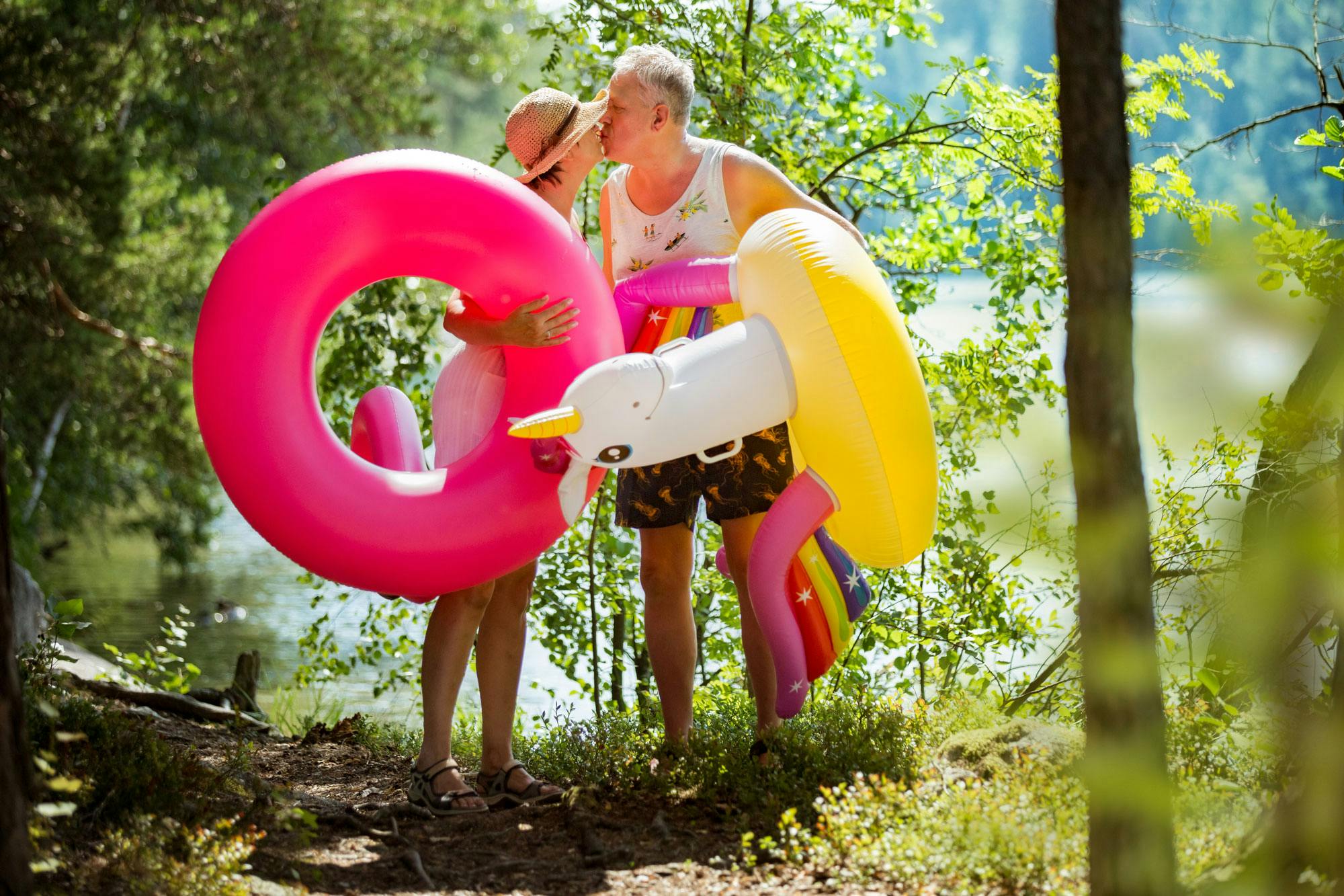 A woman and a man gently kissing while carrying inflatable water toys