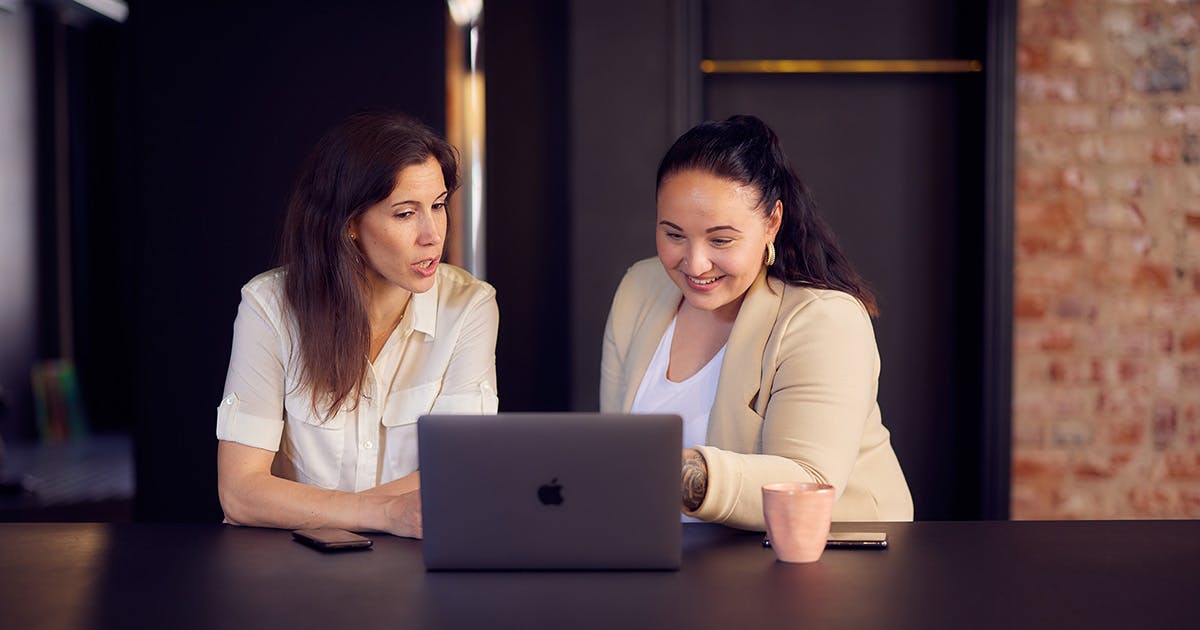 Kaksi naista keskustelee hymyillen kannettavan tietokoneen edessä. 