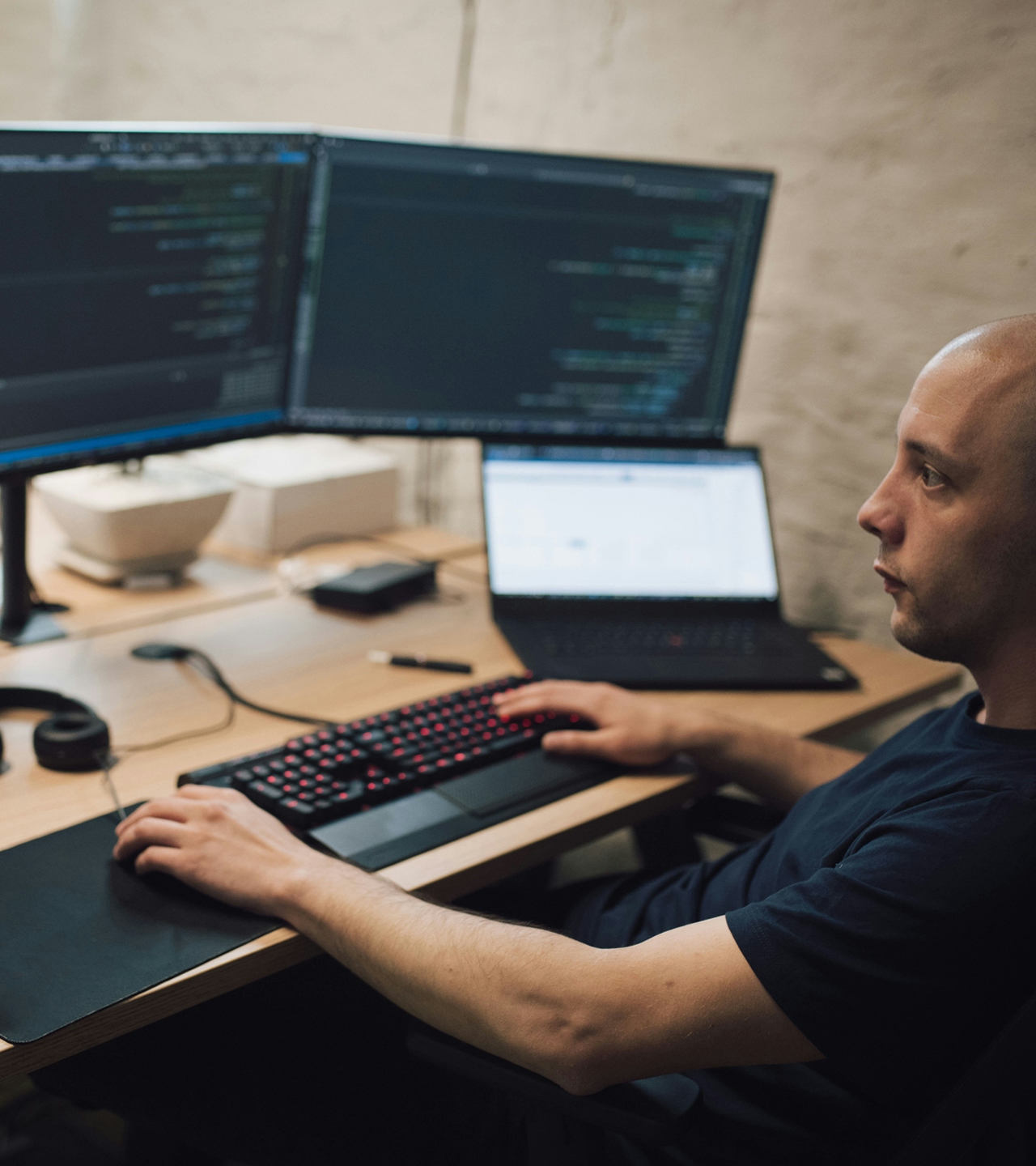 A man coding in front of three monitors and a laptop