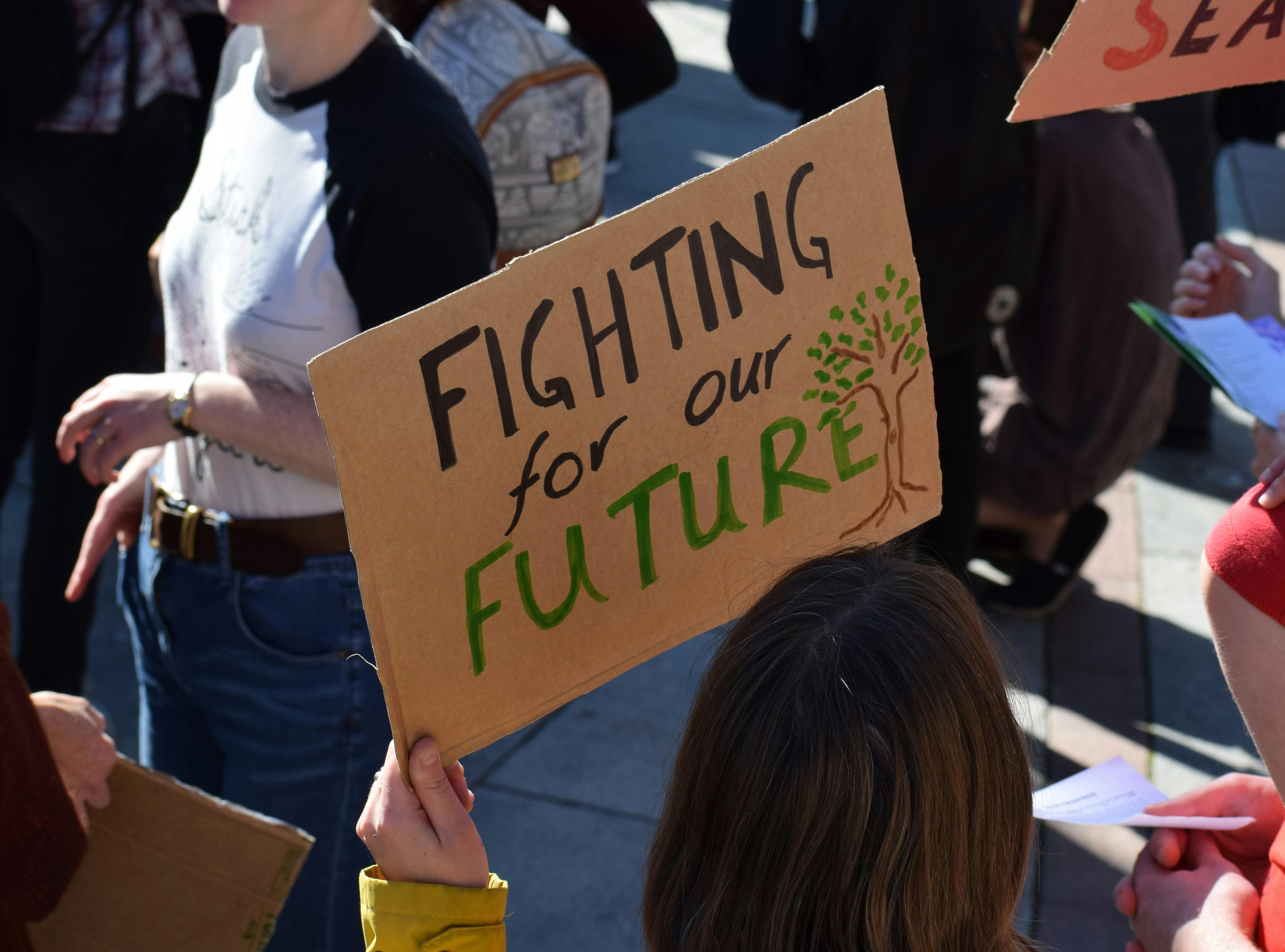 Foto von einer Demonstration. Eine Person, die nur von hinten zu sehen ist, hält ein Pappschild mit der Aufschrift "Fighting for our Future"