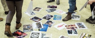 Auf dem Boden liegen für eine Assoziationsmethode Fotos aus. Man sieht die Füße und Beine von Teilnehmenden, die sich ihre Bilder aussuchen.