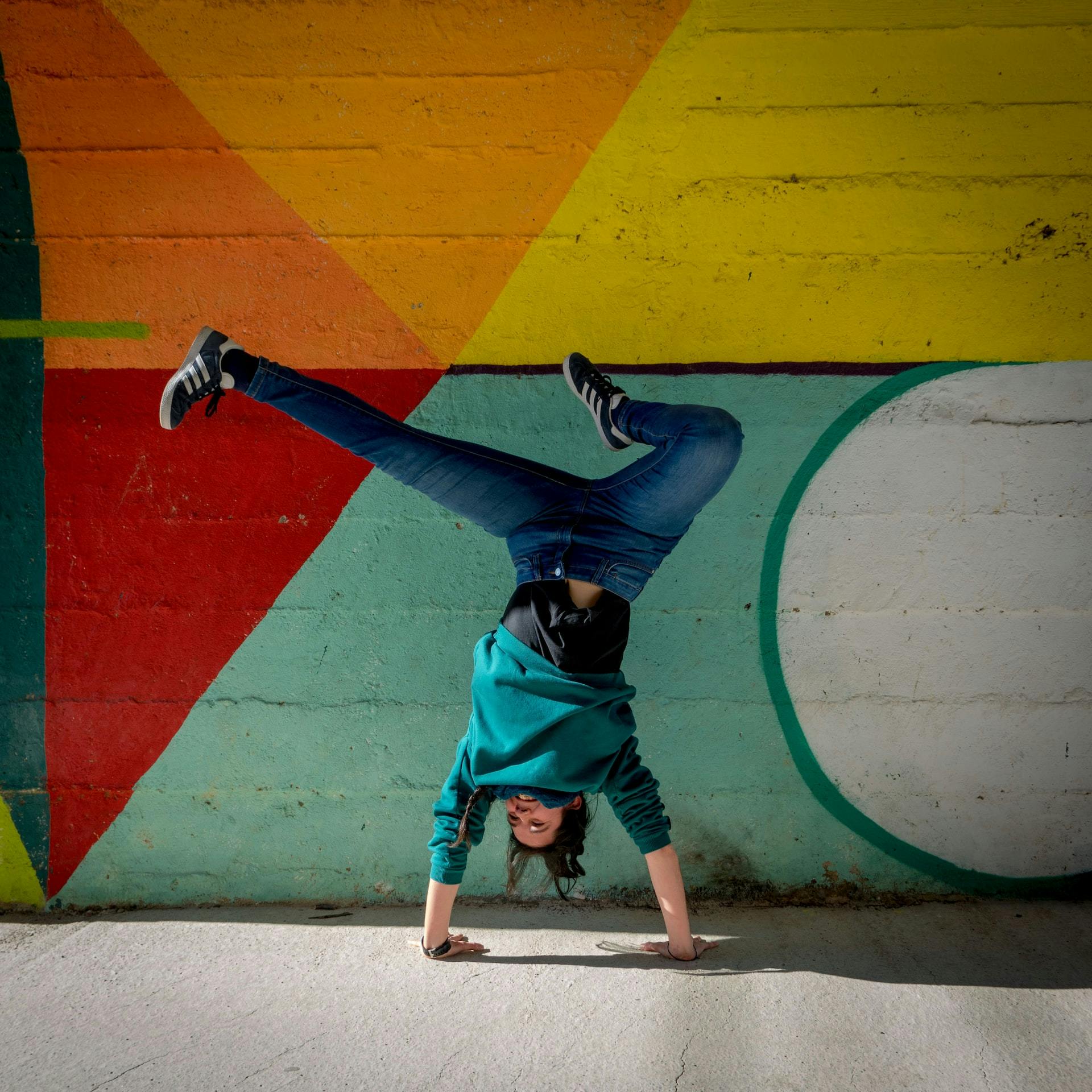 Person macht Break Dance vor bunter Wand