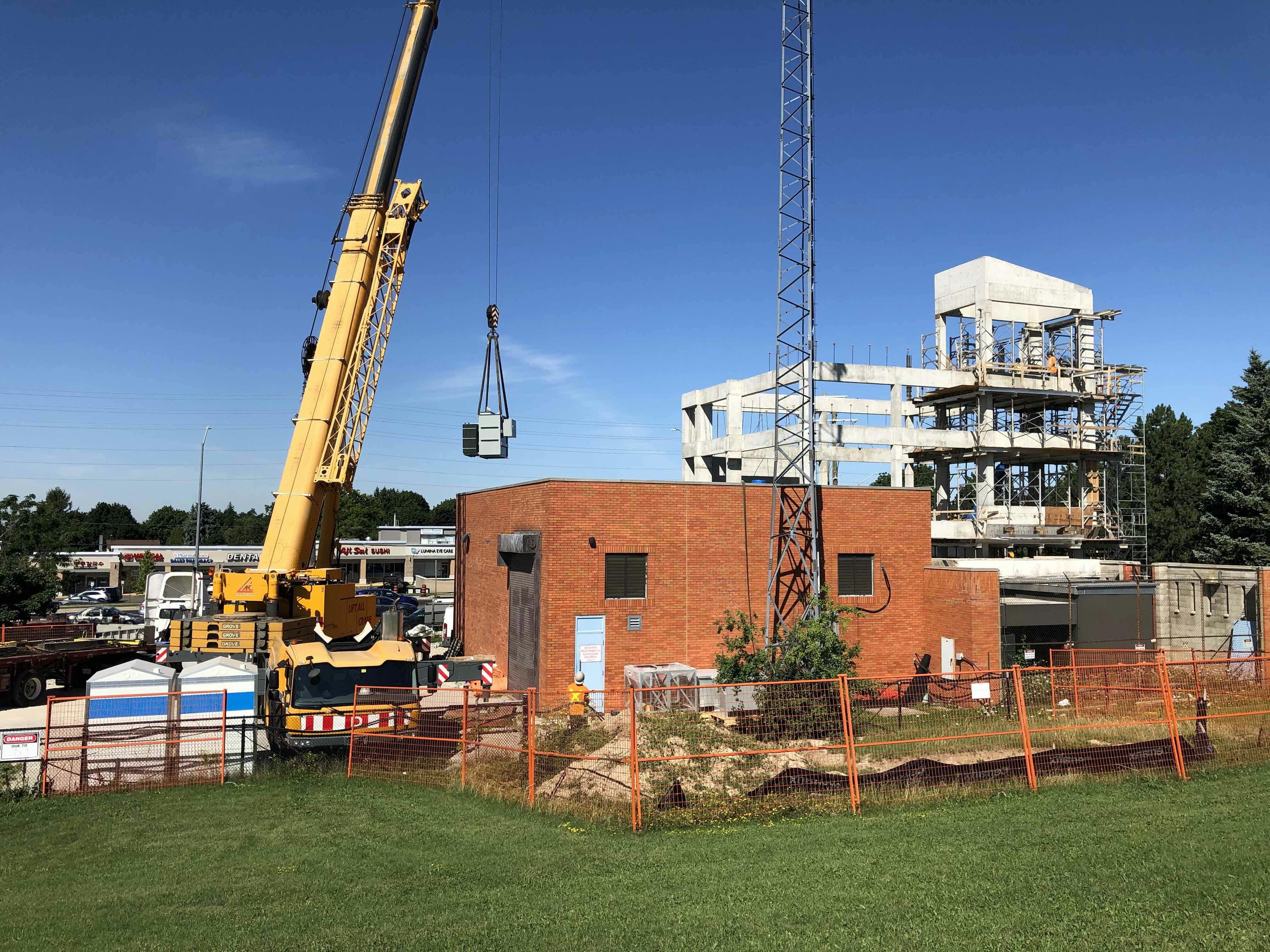 Construction site with a crane lifting materials, a red brick building, and a multi-story structure under construction in the background