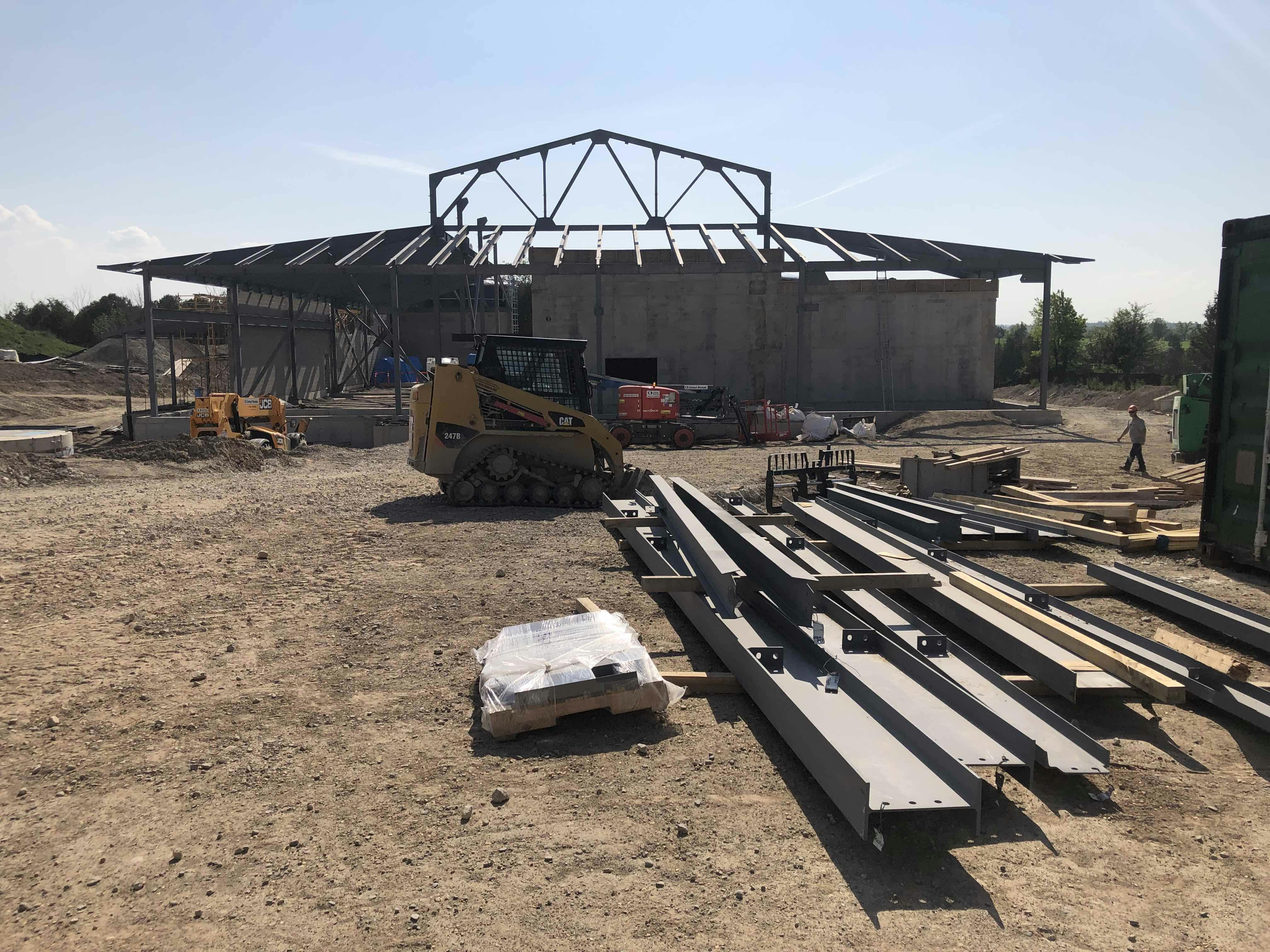 Construction site with a partially built structure, a small construction vehicle, and steel beams on the ground