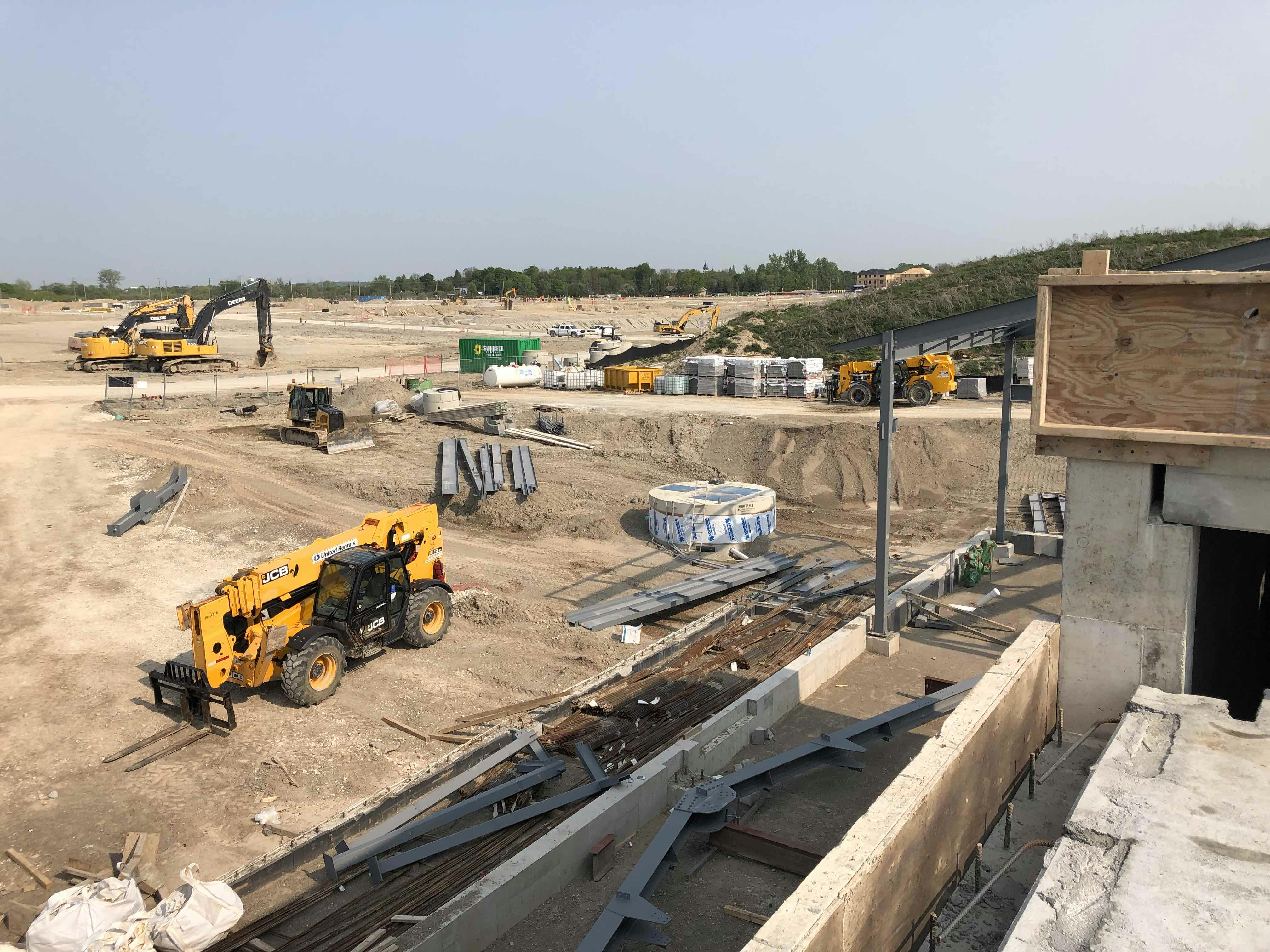 Construction site with various construction vehicles, building materials, and equipment spread across a sandy area