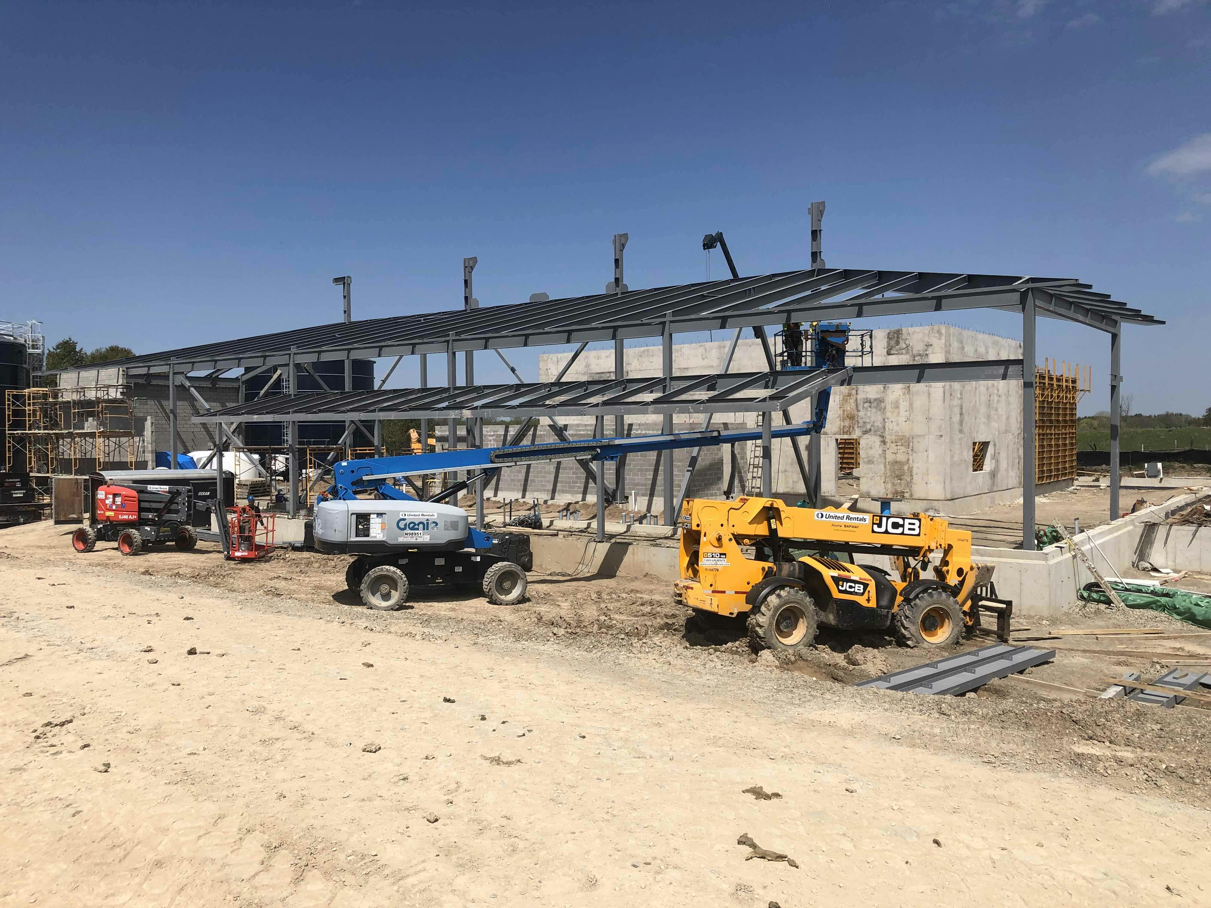 Construction site with a partially built structure, a yellow vehicle, a blue lift, and other construction equipment on a sandy ground