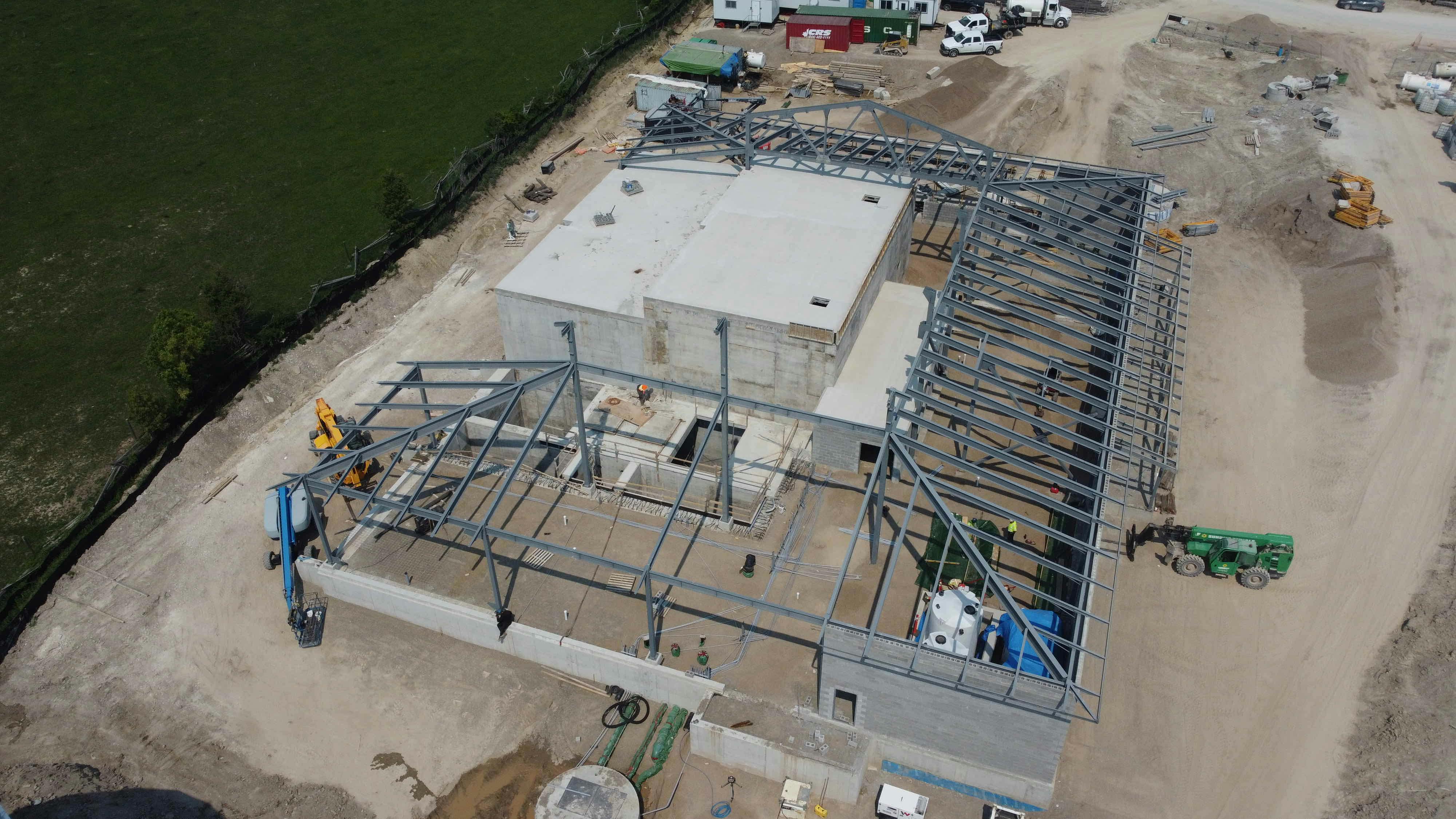 Aerial view of a construction site with a large building framework, concrete structures, construction vehicles, and surrounding dirt paths