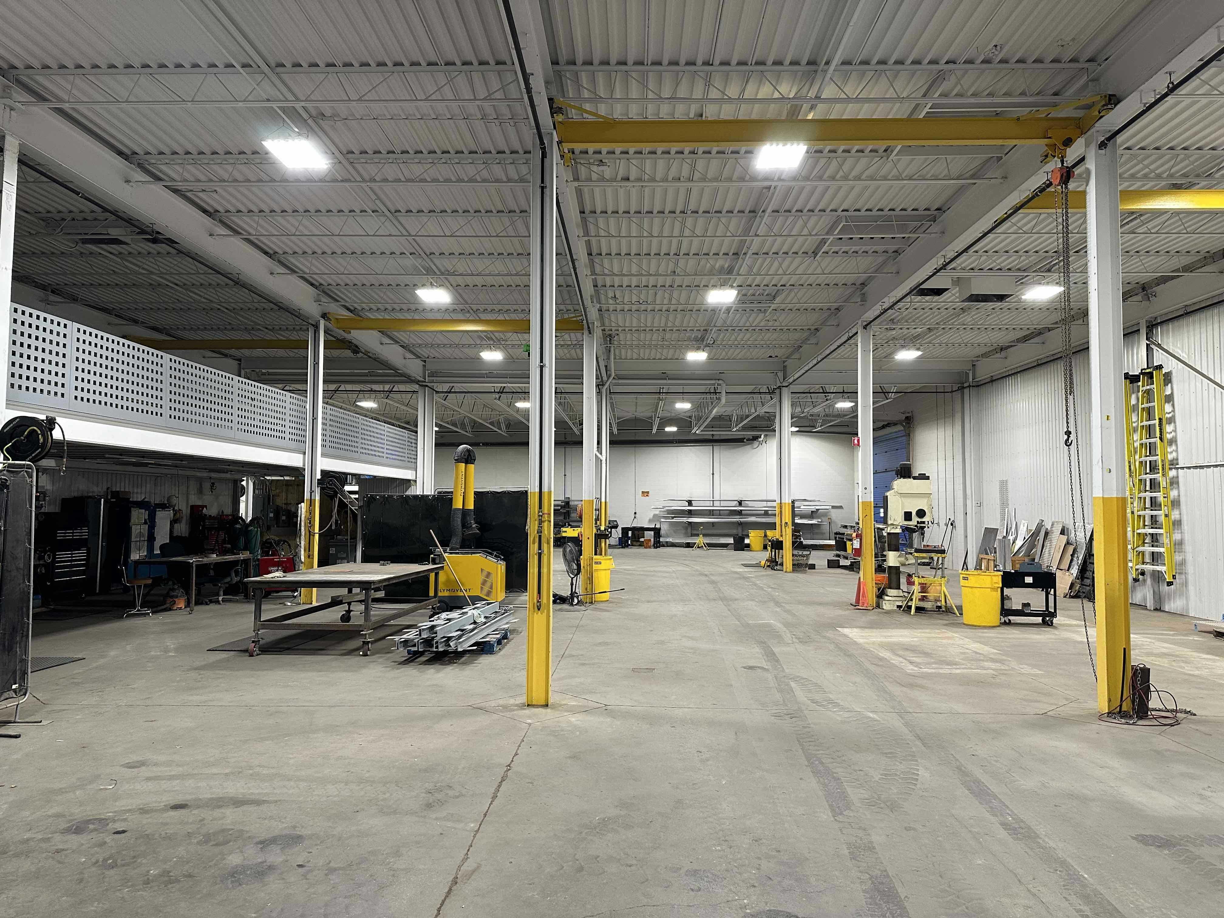 Interior view of a spacious industrial shop at Colby Drive with various workstations, equipment, and yellow pillars