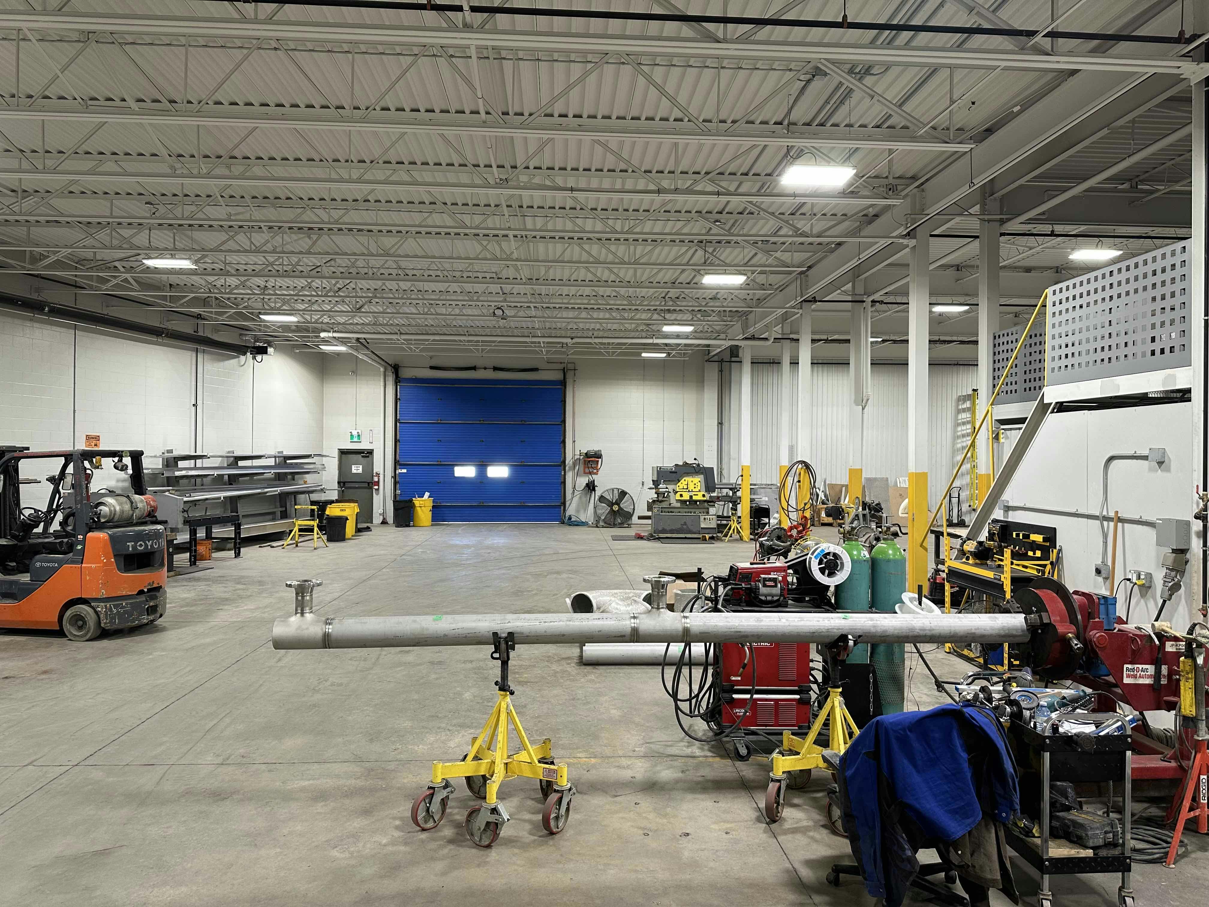 Interior view of a workshop at Colby Drive with various tools, equipment, a forklift, and a large blue door in the background