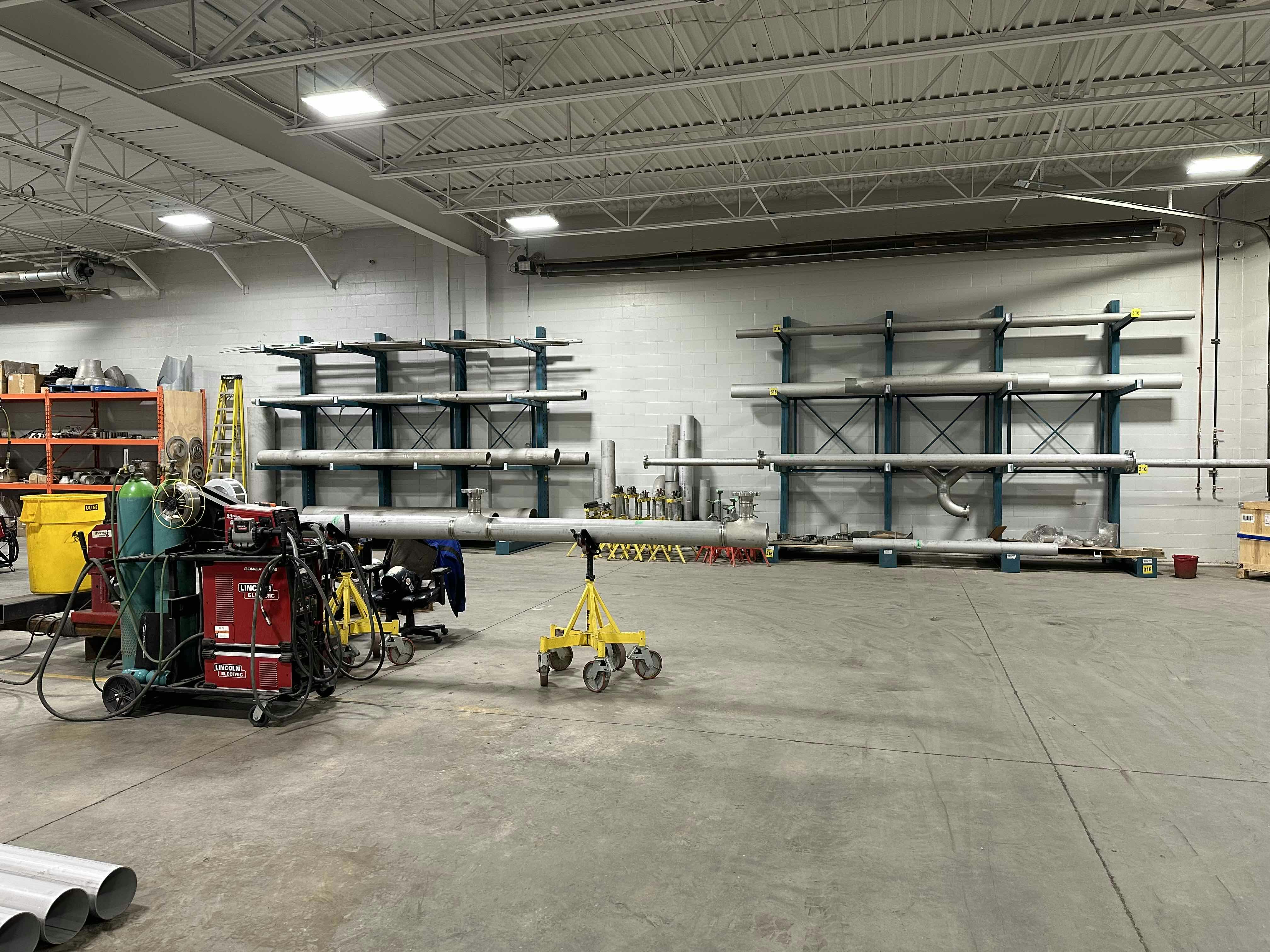 Interior view of a workshop at Colby Drive with metal pipes stored on racks, welding equipment, and other tools