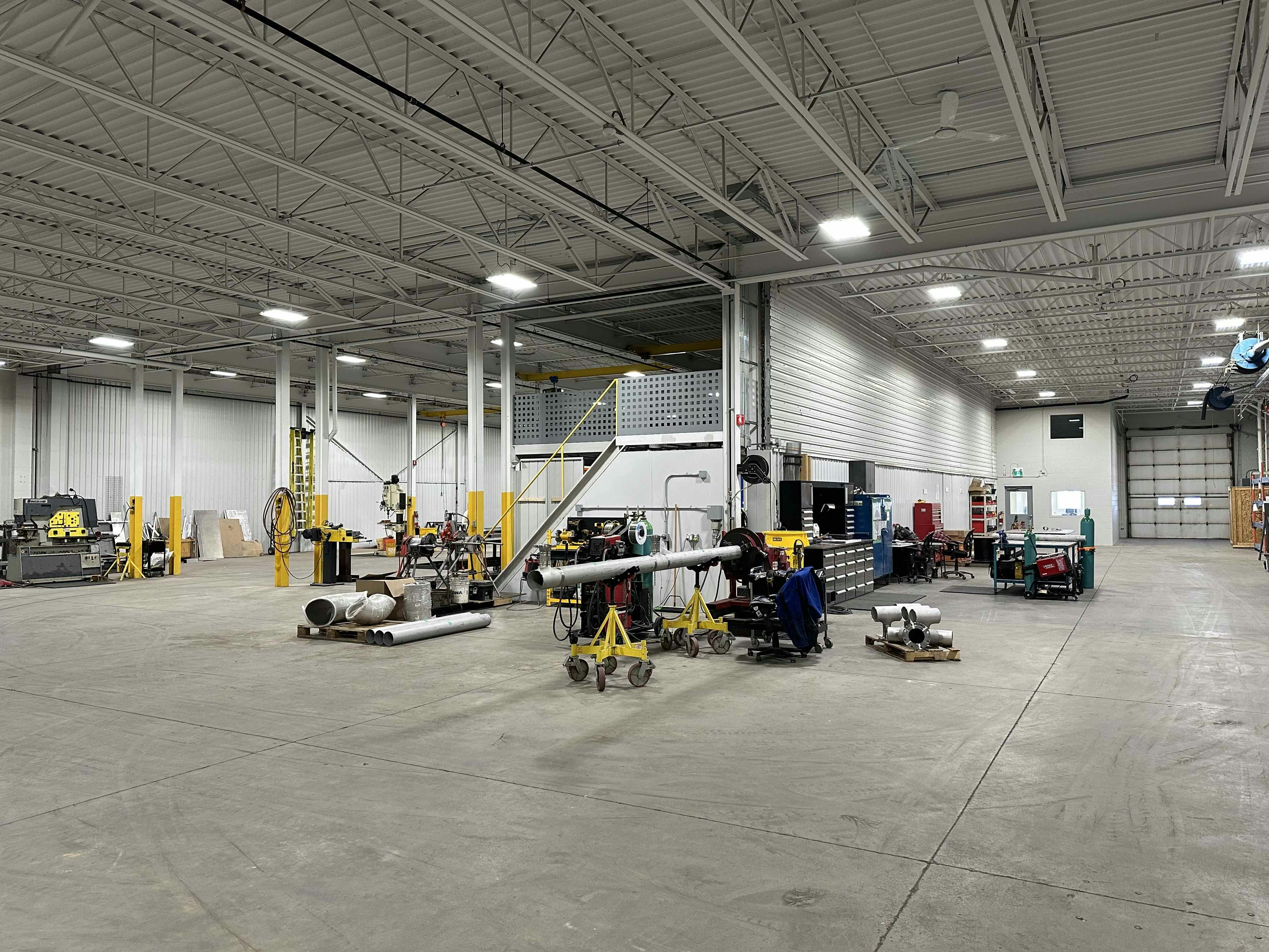 Spacious interior of a workshop at Colby Drive with various tools, equipment, metal pipes, and yellow pillars