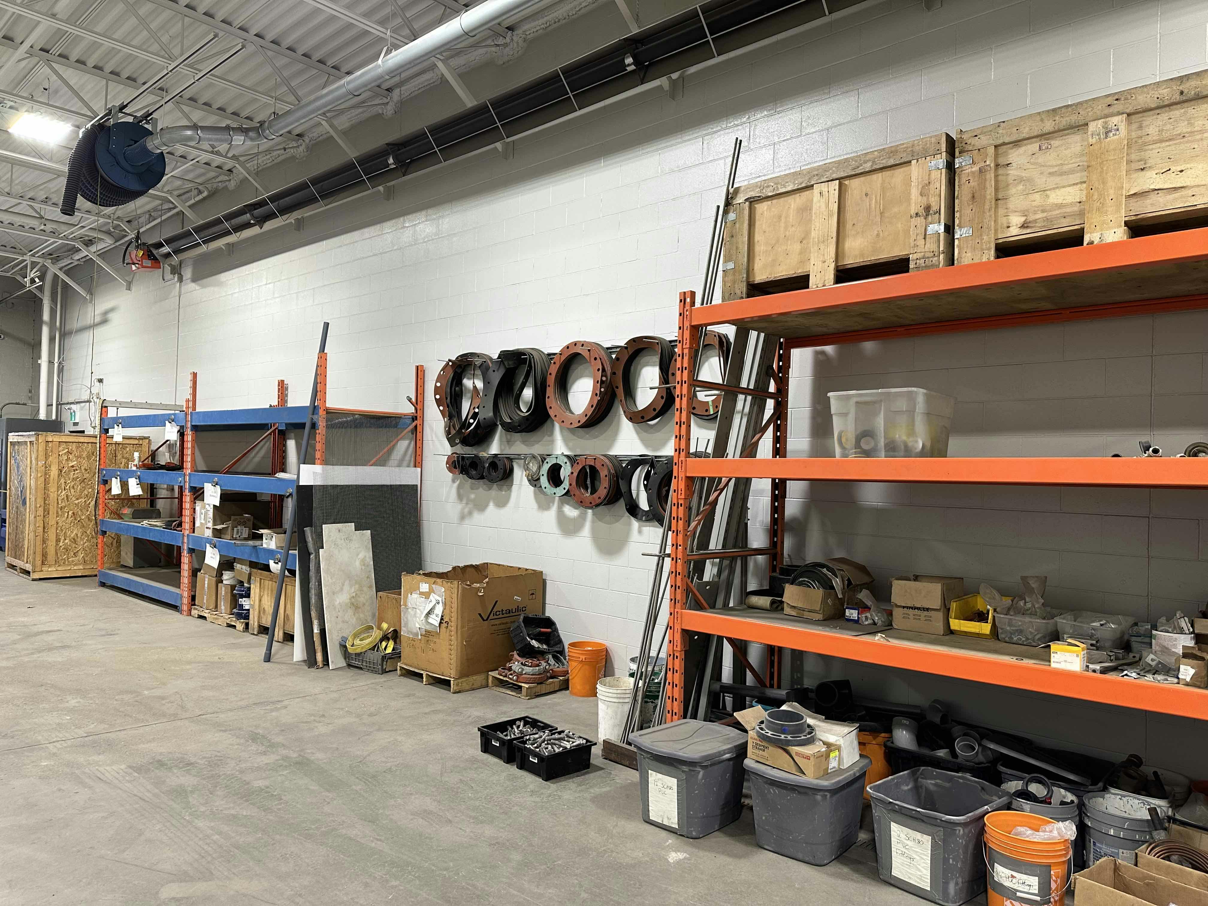 Interior view of a workshop at Colby Drive with orange storage racks holding various tools, materials, and equipment