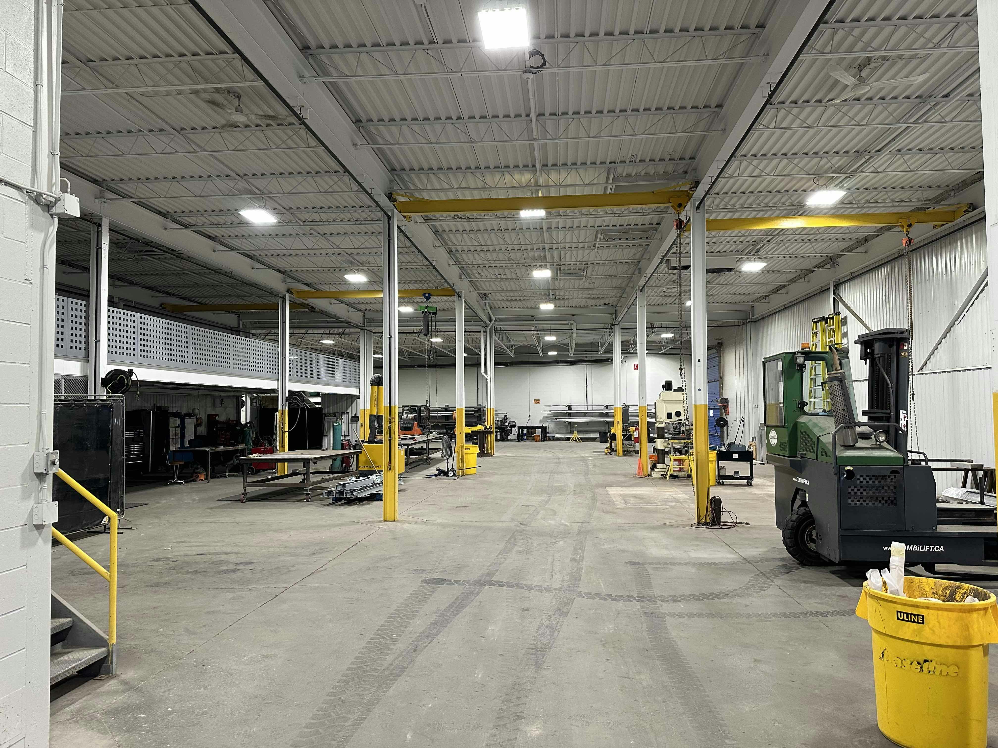 A large, open industrial warehouse with machinery, workstations, and equipment spread throughout the space