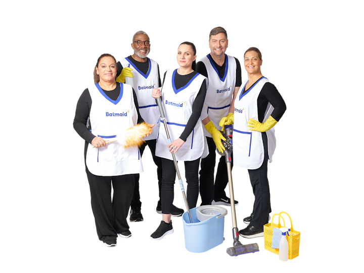 Group of diverse Batmaid cleaning staff posing together, all wearing white aprons with the Batmaid logo and holding cleaning tools.
