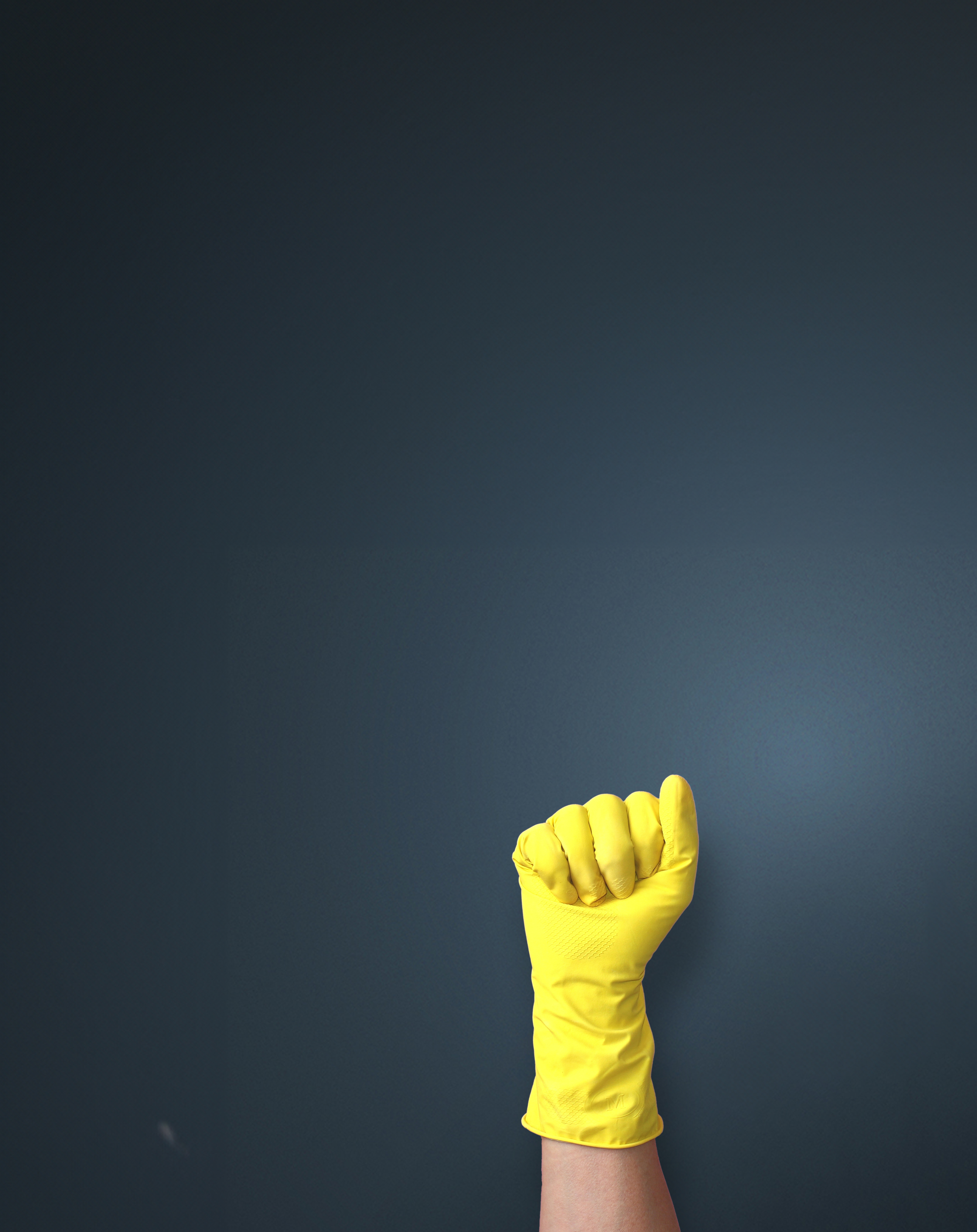 Yellow rubber glove with a clenched fist against a dark blue background, symbolizing the fight against the black market in the cleaning industry