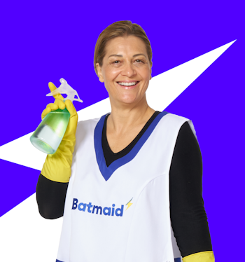 Ritratto di un'addetta alle pulizie sorridente con il grembiule di Batmaid, posando con sicurezza su uno sfondo blu scuro.