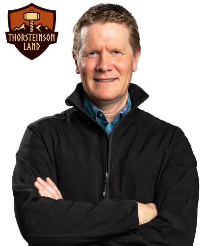 Shield badge with a farm scene including fields and a structure, labeled “Thorsteinson Land,” in brown and gold tones beside a photo of Gary Thorsteinson with his arms crossed