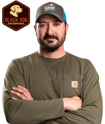 Hexagonal badge with a side profile of a dog’s head and the text “Black Dog Enterprises,” in dark brown and orange beside a photo of Nathan Kuhn with his arms crossed