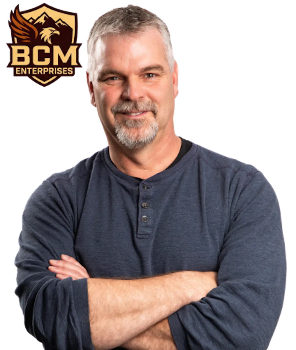 Shield badge showing a mountain and pine tree landscape with the text “BCM Enterprises” in gold and brown beside a photo of Bernie McClean with his arms crossed
