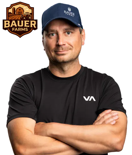 Shield badge with a barn and silo illustration at the top and “Bauer Farms” in bold lettering, using warm brown and orange hues beside a photo of Chris Bauer with his arms crossed