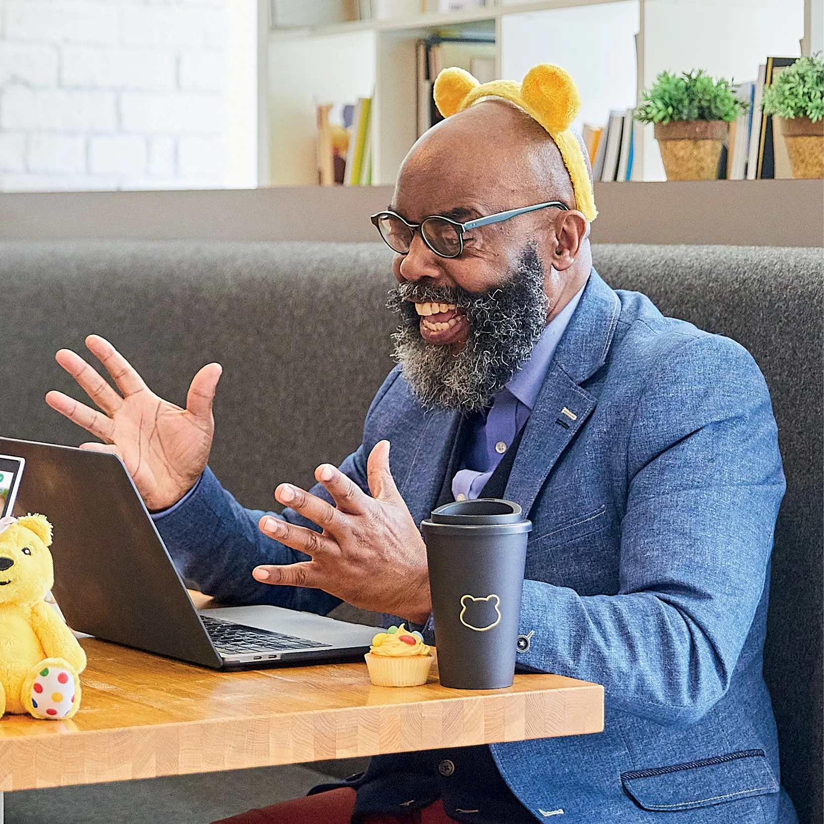 An adult sitting in front of a laptop wearing Pudsey ears.